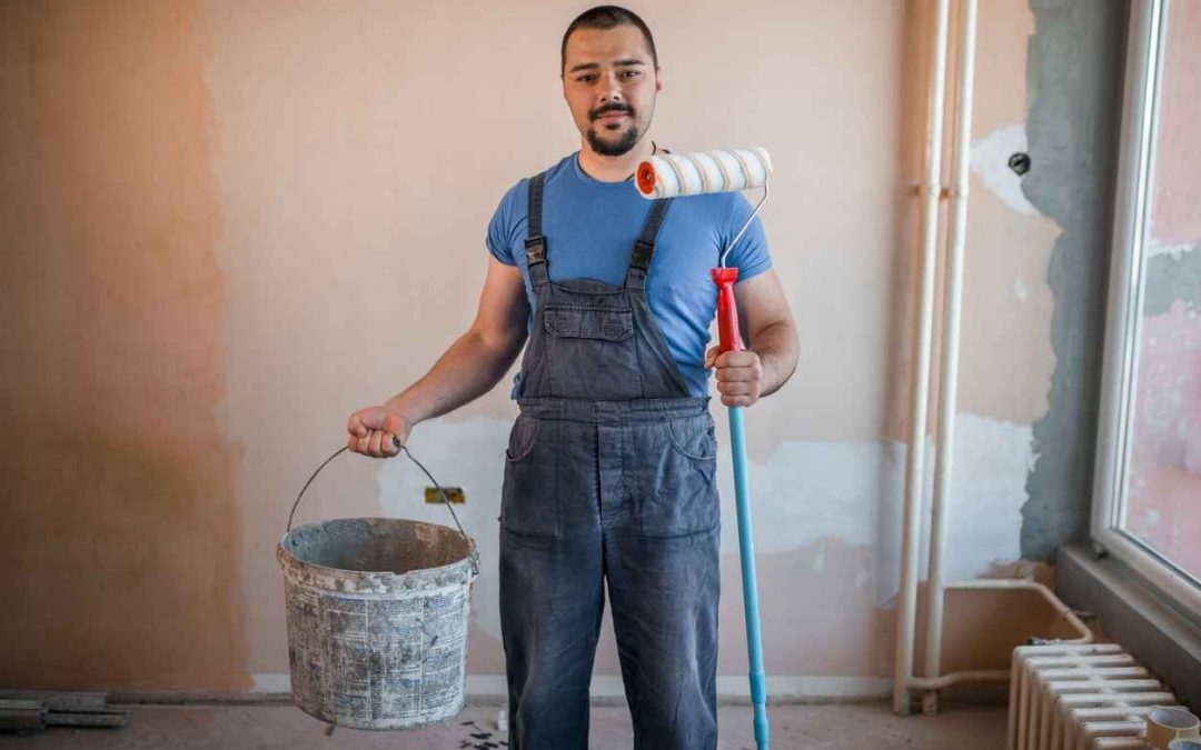 Smiling painter in coveralls holding paint roller and a bucket